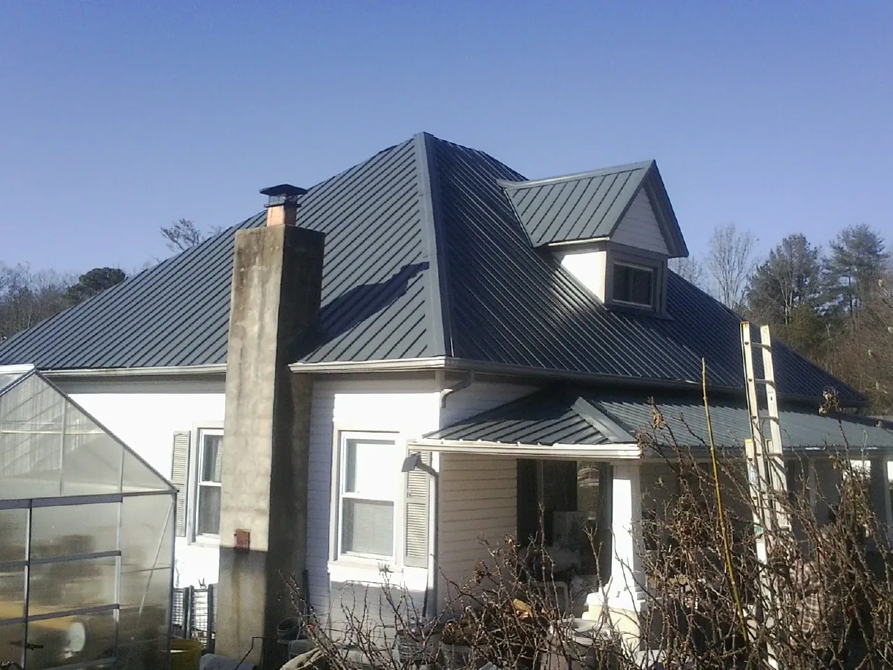 Dark blue standing seam metal roof on a white farmhouse with dormer — Slate & Tile Roof Repair by Roofing Brothers in Mount Gretna