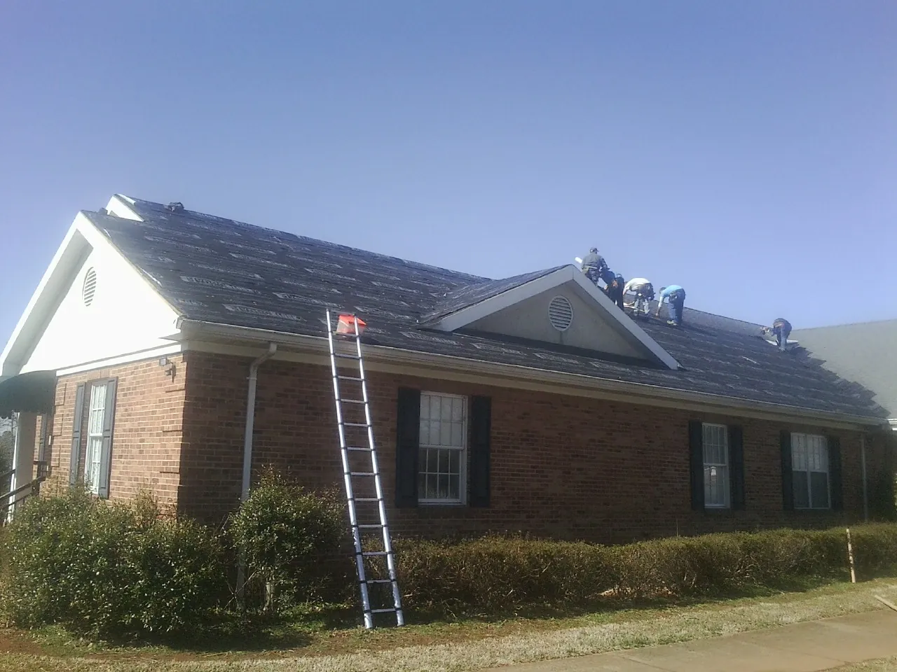 Crew tearing shingles off a brick ranch roof with a ladder set — Emergency Roof Repair work by our crew in Mount Gretna