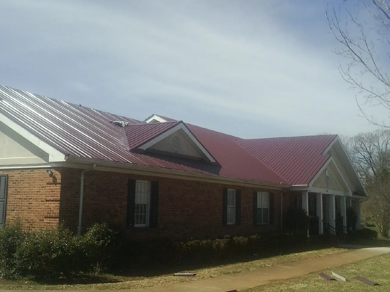 Red metal roof with gabled entries on a long brick building, from a Hail Damage Roof Repair job in Mount Gretna