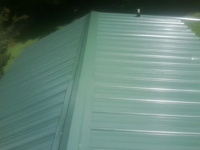 New green metal panels meeting at the ridge of a roof — Flat Roof Repair work by our crew in Mount Gretna