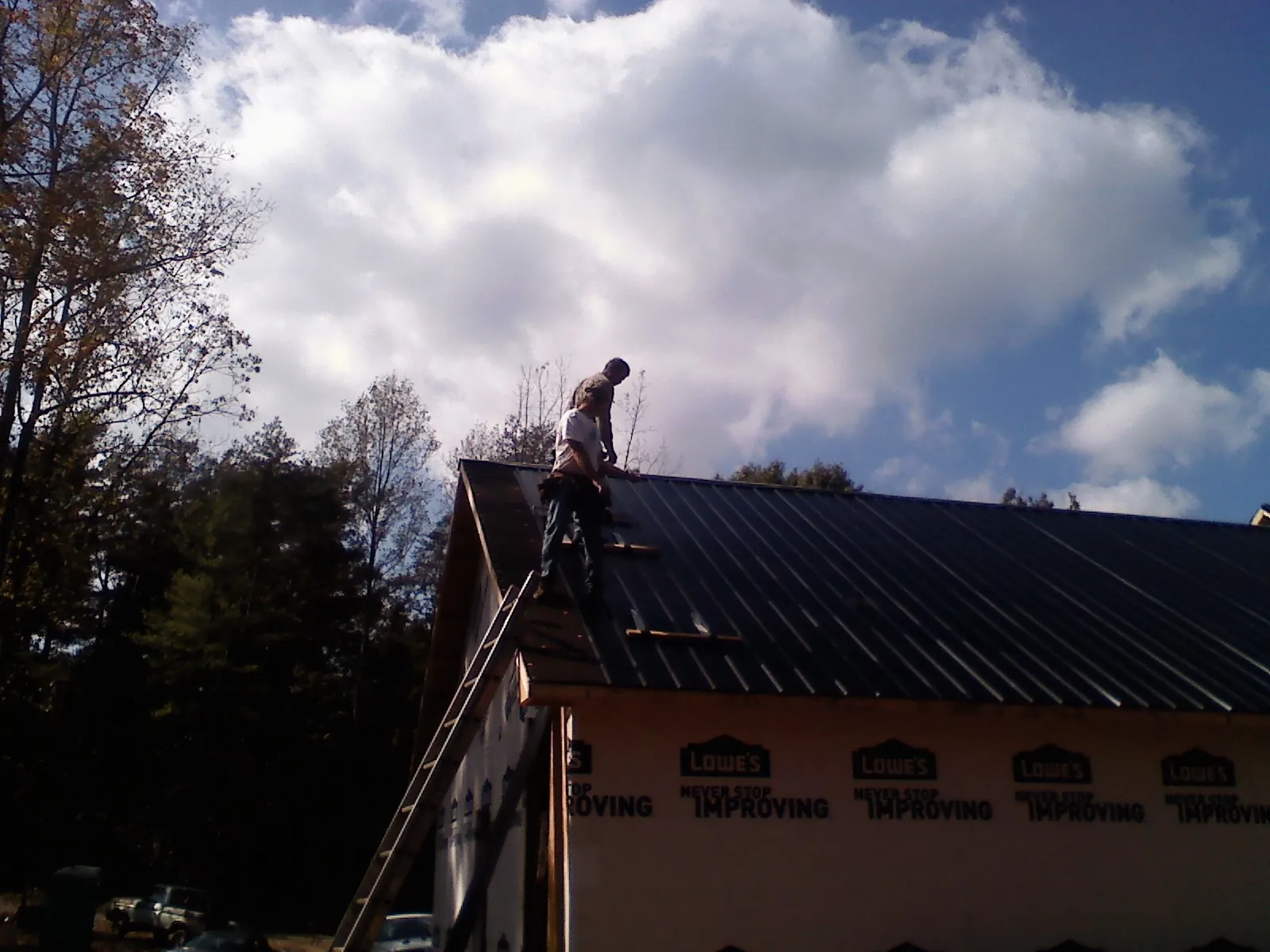 Roofer fastening dark metal panels high against a cloudy sky, from a Roof Inspection job in Mount Gretna