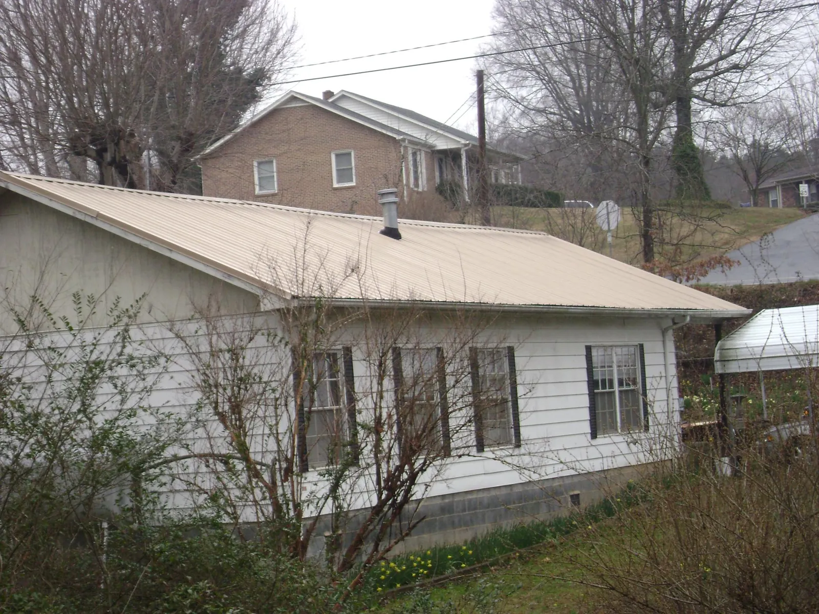 Tan metal roof on a white sided house set into a hillside — Commercial Roofing by Roofing Brothers in Mount Gretna